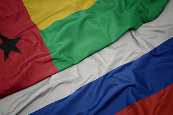 ondeando colorida bandera de Rusia y bandera nacional de Guinea Bissau
. - Foto, imagen