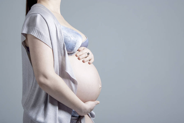 Pregnant woman on gray background in studio. - Zdjęcie, obraz