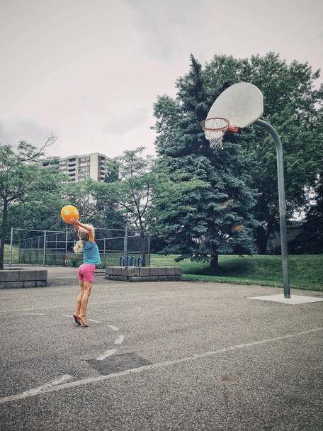 Przedszkole kaukaski dziewczyna dziecko gra w koszykówkę z pomarańczowym żółtym piłkę. Kid zabawy na zewnątrz na placu zabaw. Zdrowy styl życia letnie dzieciństwo na świeżym powietrzu aktywności sportowej. - Zdjęcie, obraz