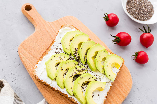 Snacks with avocado. Avocado toast with chia seeds and cream cheese, cherry tomatoes on table. Healthy breakfast lying on gray concrete background. Mockup, flat lay, top view with copy space - Photo, image