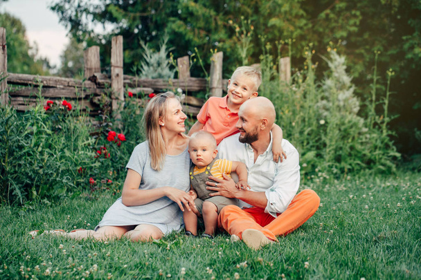 夏の日に公園で4人の美しい幸せな白人ウクライナの家族。母と父は二人の息子の兄弟を抱きしめる。ライフスタイル本物の自然な感情の瞬間.  - 写真・画像