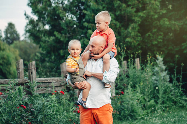 Kaukasischer Vater umarmt an einem Sommertag spielende Jungen im Park. Papa mit tragenden Kindern. authentischer Lebensstil, der zarte Momente berührt. Familienleben glückliches Vaterschaftskonzept.  - Foto, Bild
