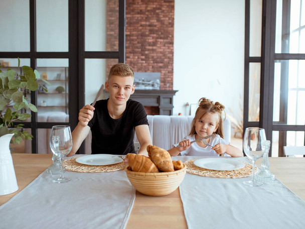 kafkas komik sevimli kardeşler -modern çatı iç yemek odasında ağabeyi ile küçük kız. Aile, yaşam tarzı ve yeme konsepti - Fotoğraf, Görsel