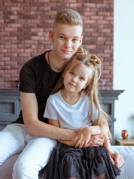 caucasian siblings - teenager boy brother and little girl sister sitting on a couch (sofa) in modern loft interior - Photo, image