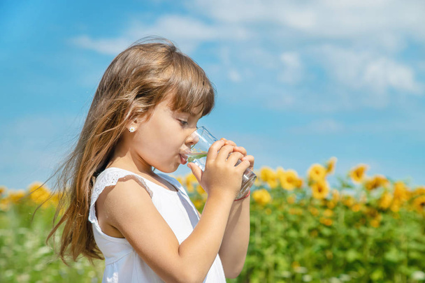 ein Kind trinkt Wasser auf dem Hintergrund des Feldes. Selektiver Fokus. - Foto, Bild
