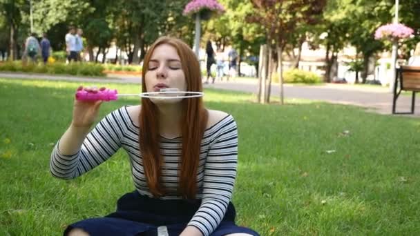 Chica pelirroja sopla burbujas de jabón en el parque Ella sonriendo y riendo verano y felicidad Slow Motion
 - Metraje, vídeo
