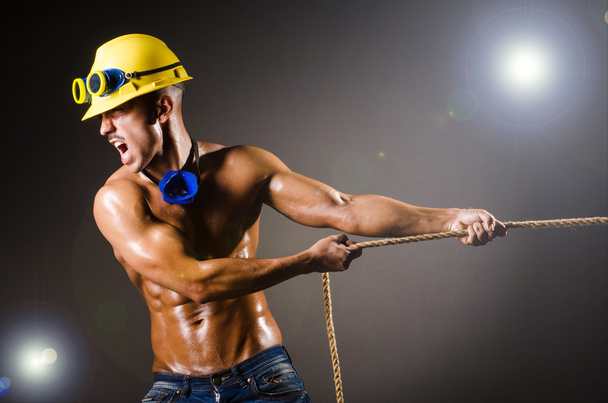 Constructor desnudo tirando de la cuerda en la oscuridad
 - Foto, Imagen
