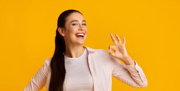 Positive Young Woman Showing OK Gesture Over Yellow Background - 写真・画像