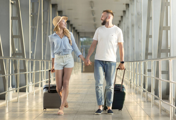Couple holding hands, walking at covered passage in airport - 写真・画像