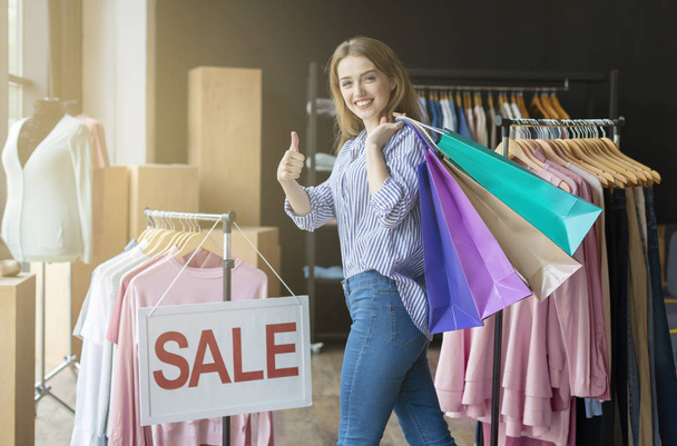 glücklicher Shopaholic, der Einkaufstüten auf der Schulter trägt und Daumen nach oben zeigt - Foto, Bild