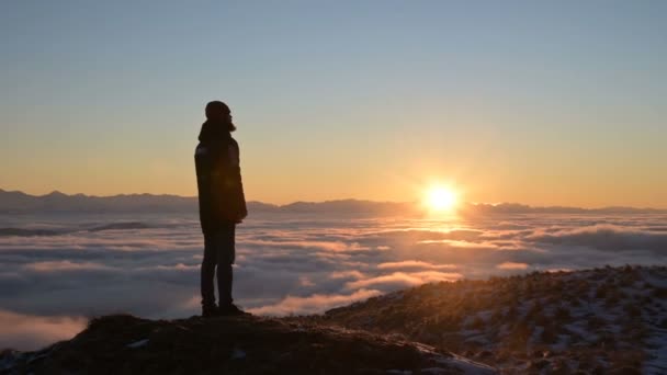 The silhouette of a man stands at sunset above the clouds and contemplates the setting sun. The concept of tranquility and pleasure in traveling - Footage, Video
