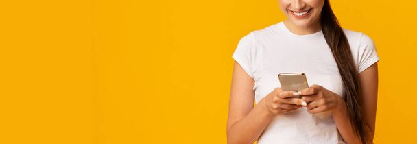 黄色のスタジオの背景に携帯電話を使用してミレニアル世代の女の子, トリミング - 写真・画像