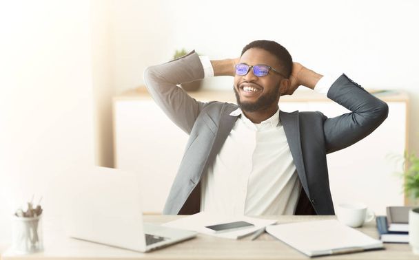 Африканский бизнесмен отдыхает в офисе, сидит с руками за головой
 - Фото, изображение