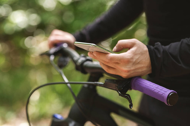 Ritagliato imafe di ciclista in possesso di bici e utilizzando smartphone
 - Foto, immagini