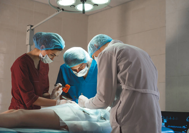 Группа хирургов за работой в хирургическом театре. Команда реаниматологов в защитных масках
 - Фото, изображение