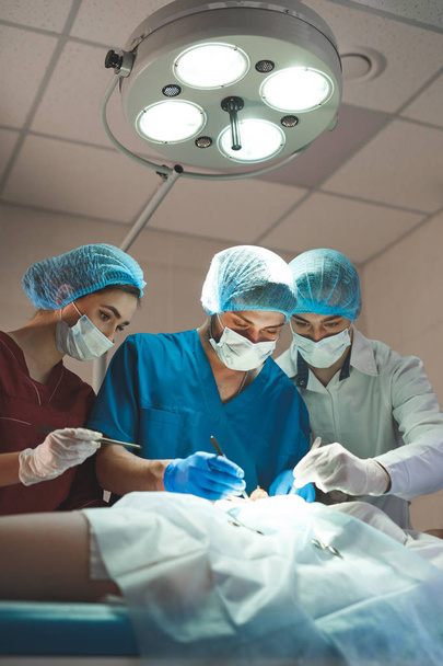 Group of surgeons at work operating in surgical theatre. Resuscitation medicine team wearing protective masks - Foto, imagen