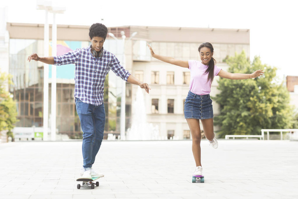 Cheerful teenagers racing on skateboards against cityscape - Foto, afbeelding