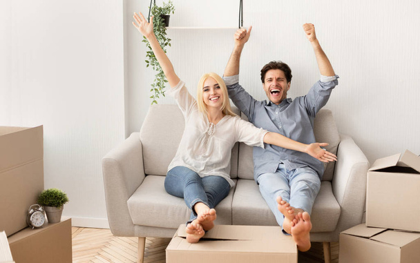 Fröhliches Paar entspannt auf Sofa und feiert Umzug ins neue Haus - Foto, Bild