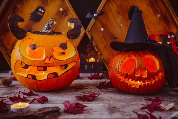 Két faragott tök és más szimbólumok a Halloween a fából készült háttér. Halloween tök fej Jack lámpa félelmetes gonosz arcok. Kísérteties ünnep fogalmát. Lemezterület másolása. - Fotó, kép