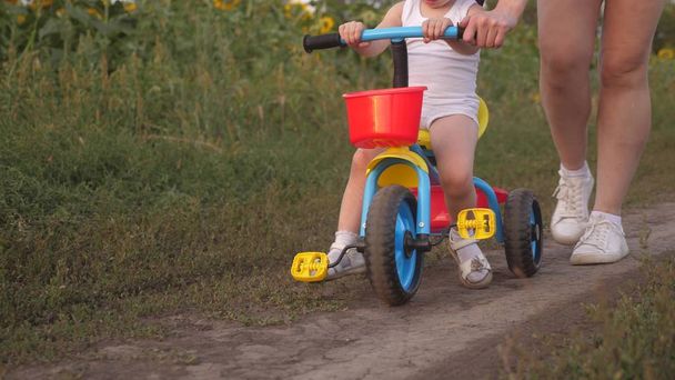 Mom teaches daughter to ride a bike. close-up. Mother plays with her little daughter. a small child learns to ride a bike. concept of happy childhood. - Photo, Image