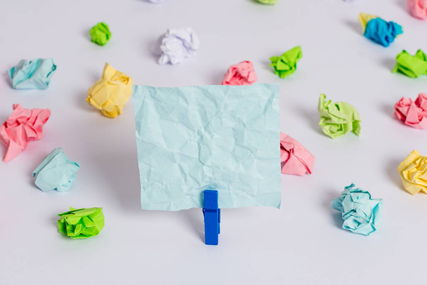 Colored crumpled sheets placed around the empty rectangle square shaped reminder note in the centre of a white floor. Office supplies, blank paper pinned by a fastener. - Photo, Image