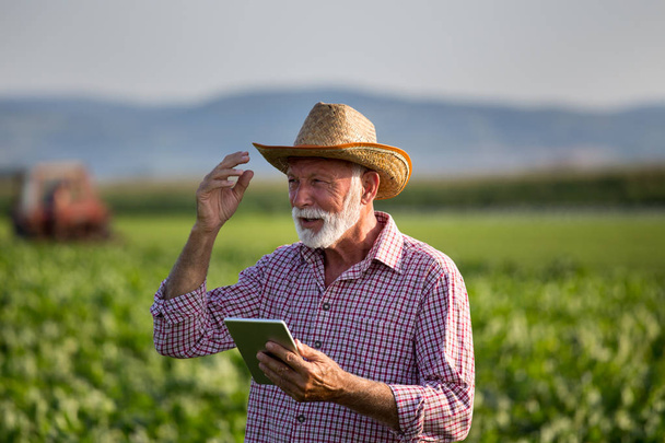 Agricultor con tableta delante del tractor en el campo
 - Foto, imagen