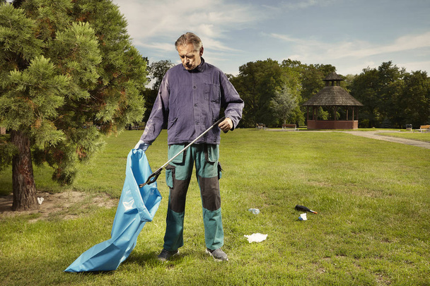 Man in public service cleaning up trash in city park - Zdjęcie, obraz
