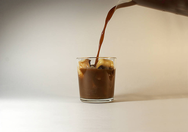 Pour cold coffee with milk in a glass, ice cubes. - Foto, imagen