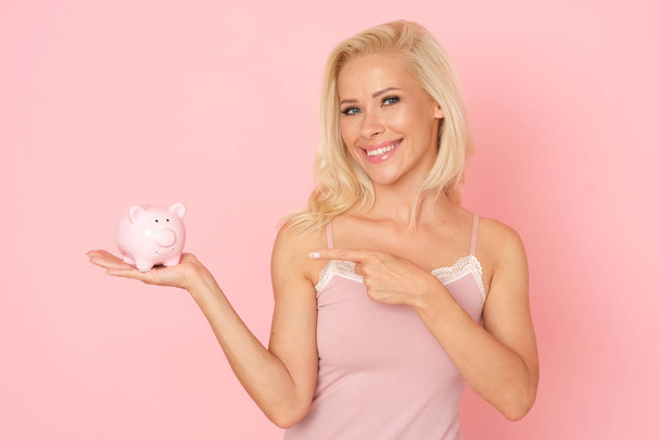 Mulher loira bonita está economizando dinheiro em seu porquinho de porcelana
. - Foto, Imagem