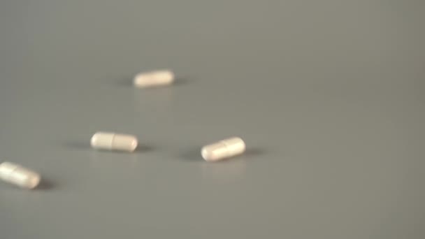White medical capsules slide down the gray coating. Glutamate sodium supplementation concept. Slow motion - Felvétel, videó