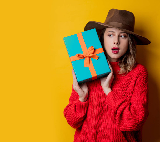 Jonge verrast vrouw in rode trui met geschenk doos - Foto, afbeelding