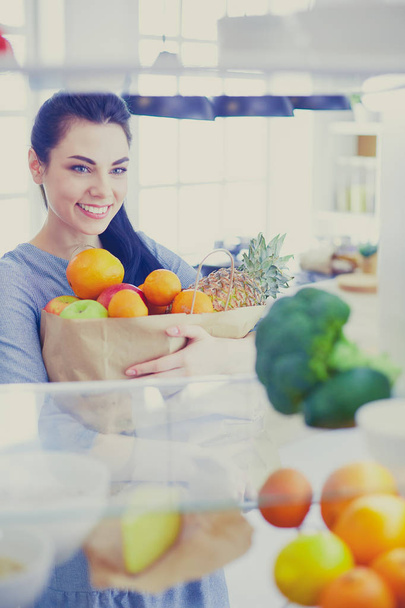 Smiling woman taking a fresh fruit out of the fridge, healthy food concept - Фото, изображение