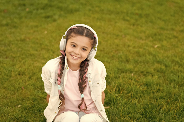 Girl with headphones nature background. Positive influence of music. Child girl enjoying music modern earphones. Childhood and teenage music taste. Little girl listening music enjoy favorite song - Foto, Bild