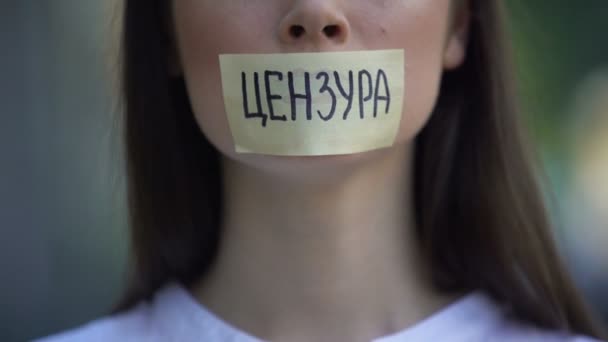 Woman resolutely taking off tape with censored word in russian over mouth - Felvétel, videó