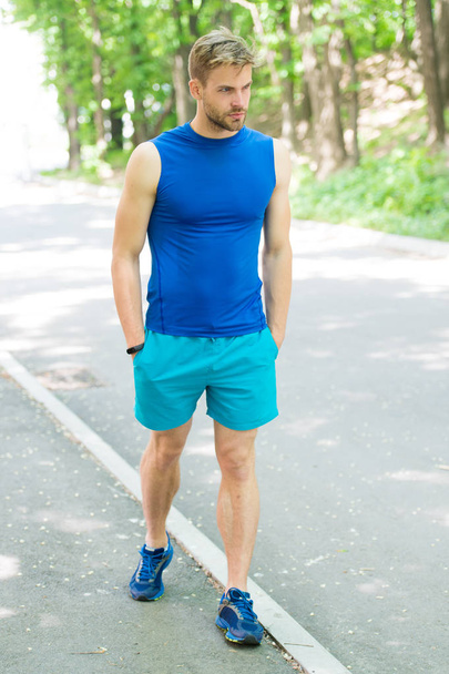 He is quite sporty. Athletic man walking on natural landscape. Handsome man with unshaved face hair and stylish haircut training outdoor. Caucasian man in sportswear on summer day - Fotó, kép
