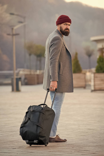 Carry travel bag. Man bearded hipster travel with luggage bag on wheels. Adjust living in new city. Traveler with suitcase arrive airport railway station urban background. Hipster ready enjoy travel - Photo, image