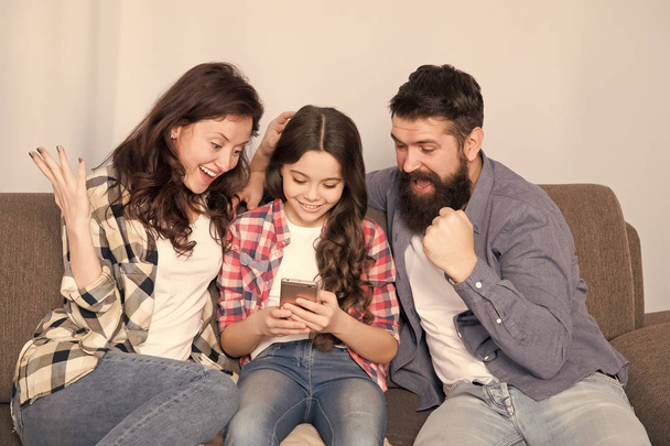 Child share news with mother and father. Little girl child use mobile phone with parents. Happy family at home. Child with childhood happiness. bearded man and woman with child. So much fun - Foto, Imagem