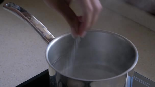 Voeg zout toe aan kokend water in een metalen pan close-up - Video