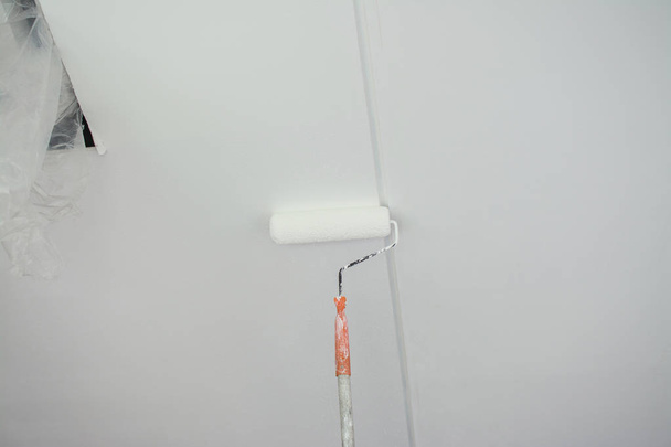 βάφοντας ένα λευκό γύψινο ταβάνι γύψο με ρολό βαφής  - Φωτογραφία, εικόνα