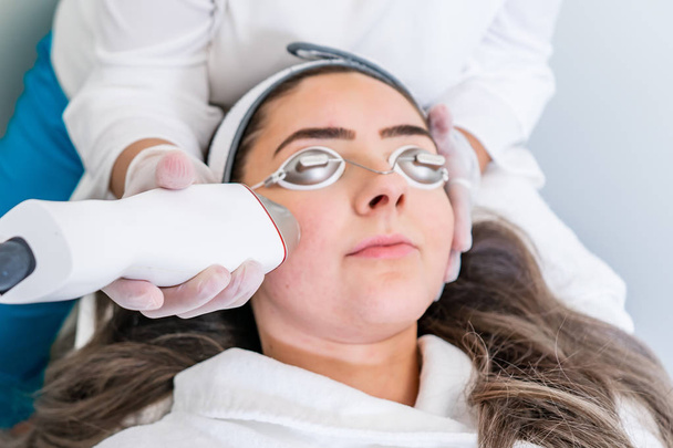 Beautician applying radio frequency microneedling handpiece to a woman's face for skin tightening treatments at a beauty clinic. - Photo, Image