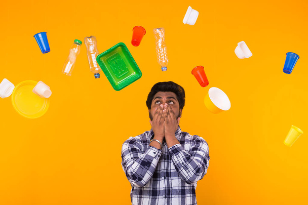 Environmental pollution, plastic recycling problem and ecology problem concept - sad indian man is upset because is got too much of plastic on the planet on yellow background. - Фото, изображение