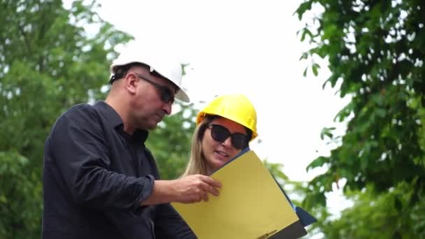 Two construction engineers, a man and a woman, wearing protective helmets inspecting the construction site and checking the projects - Footage, Video
