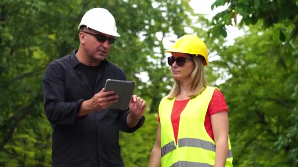 Deux ingénieurs en construction absorbés, un homme et une femme, portant des casques de protection inspectant le chantier à l'aide d'une tablette numérique
 - Séquence, vidéo