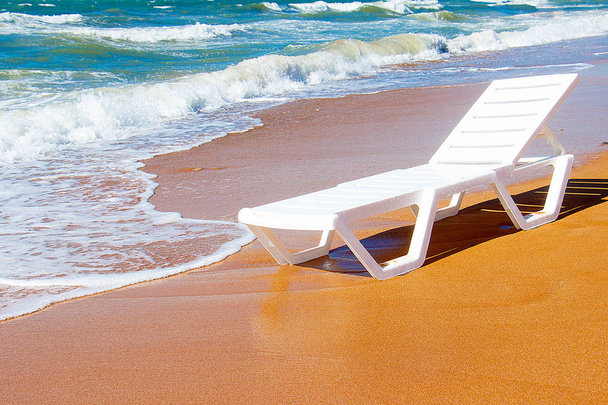 Λευκή καρέκλα σαλονιού που στέκεται σε μια αμμώδη παραλία δίπλα στη θάλασσα - Φωτογραφία, εικόνα