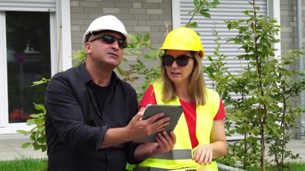 Двоє інженерів-будівельників, чоловік і жінка, одягнені в захисні шоломи, оглядають будівельний майданчик за допомогою цифрового планшетного комп'ютера
 - Кадри, відео
