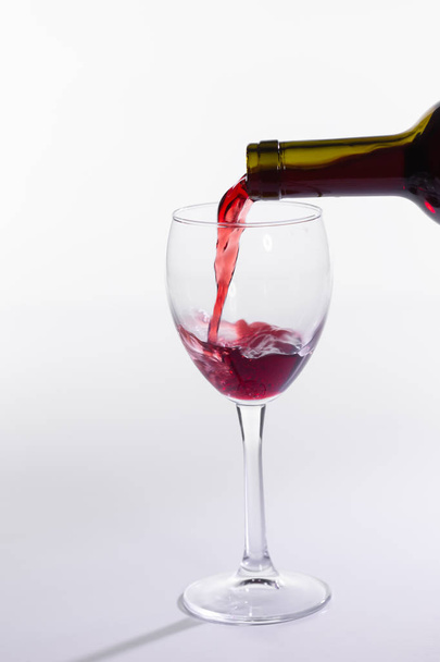 Rode wijn gieten van fles in groot glas op witte achtergrond - Foto, afbeelding