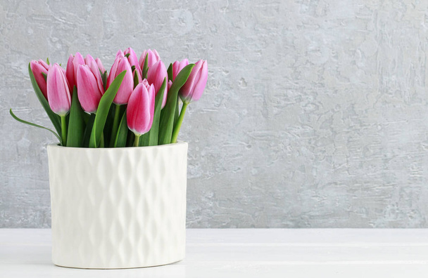 Pink tulips in white ceramic vase, grey stone background.  - Foto, afbeelding