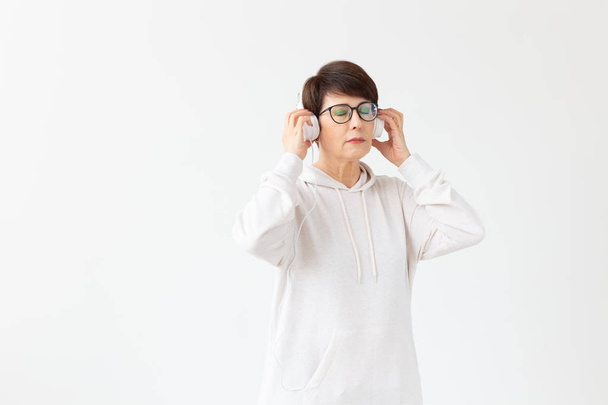 Хобі, інтереси та концепція людей - Красива жінка 40-50 років слухає музику у великих навушниках на білому тлі з місцем для тексту
 - Фото, зображення