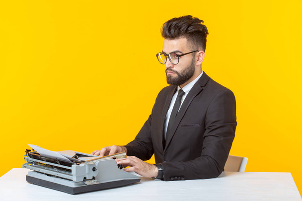 Młody przystojny mężczyzna biznesmen w formalnych ubrań wpisując tekst na maszynie do pisania stwarzających na żółtym tle. Miejsce na reklamę. Koncepcja biznesowa. - Zdjęcie, obraz