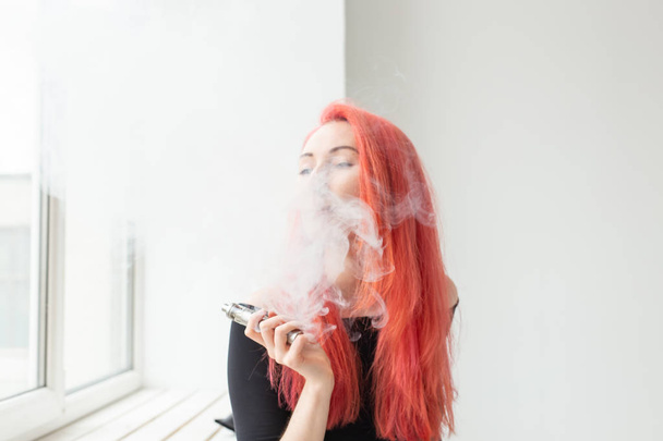 Vape, Sucht und People-Konzept - junge Frau mit gefärbten Haaren raucht einen Vape - Foto, Bild